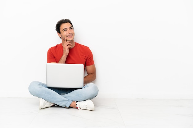 Blanke knappe man met een laptop die op de grond zit en een idee bedenkt terwijl hij omhoog kijkt