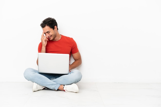 Blanke knappe man met een laptop die op de grond zit te lachen