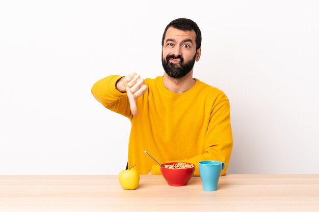 Blanke man aan het ontbijten in een tafel met duim omlaag met negatieve uitdrukking.