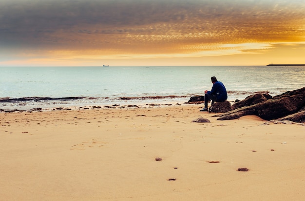 Foto blanke man alleen zittend op de oever van de zee