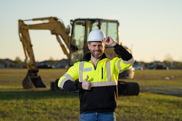 Blanke man bouwvakker in helm op bouwplaats Industrie-ingenieur in veiligheidshelm in de buurt van bulldozer of graaftractor Concept van de bouwsector Bouwplaatsmanager