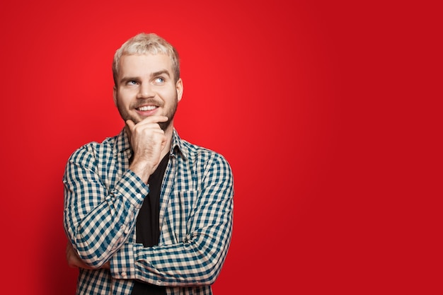 Blanke man die het idee kreeg en opzij poseert op een rode muur met vrije ruimte die zijn kin en glimlach aanraakt