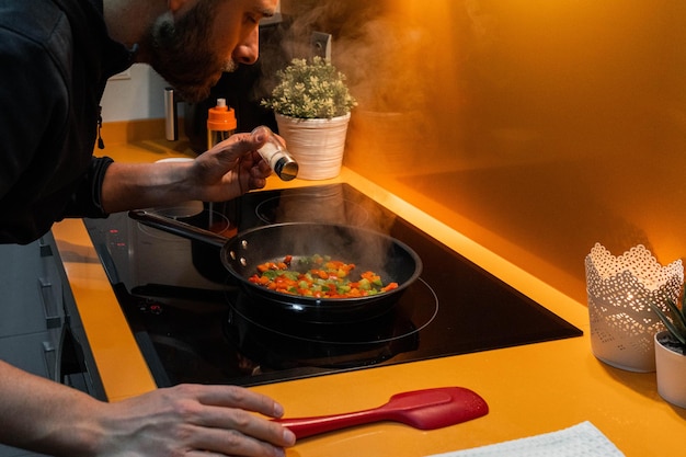 Blanke man gooit zout en kookt groenten in een koekenpan