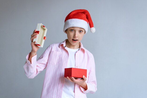 Blanke man in kerstman hoed en shirt opent cadeau en kijkt verrast op een lichte achtergrond...