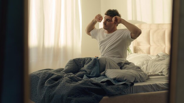 blanke man man ligt op bed wakker strekken wrijven ogen mannelijke huis slaapkamer goedmorgen slaperig