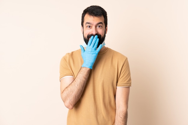 Blanke man met baard beschermen met een masker en handschoenen over geïsoleerde muur gelukkig en lachend die mond met de hand