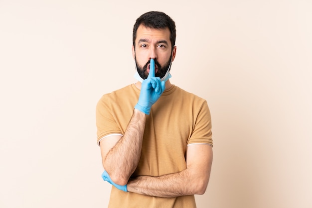 Blanke man met baard die met een masker en handschoenen over muur beschermt die een teken van stiltegebaar toont dat vinger in mond zet