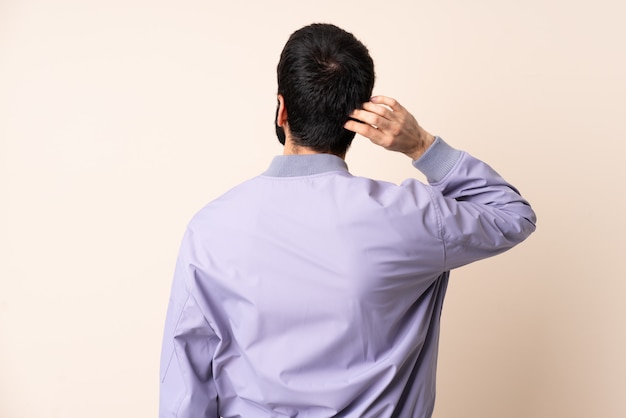 Blanke man met baard draagt een jas over muur in achterste positie en denken