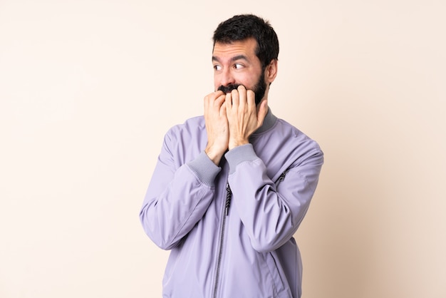 Blanke man met baard het dragen van een jas over geïsoleerde nerveus en bang handen naar mond brengen