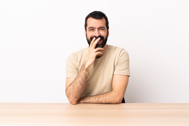 Blanke man met baard in een tafel blij en lachend die de mond bedekt met de hand.