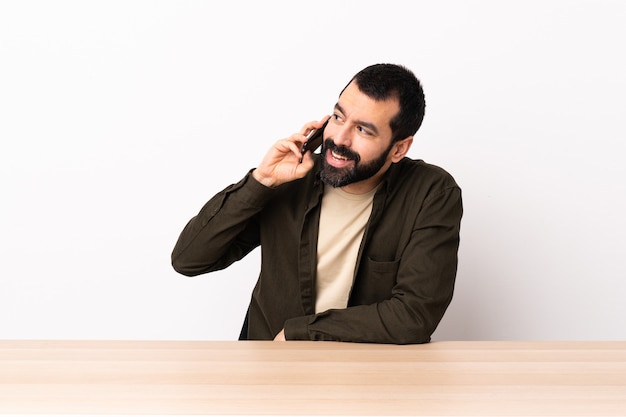 Blanke man met baard in een tafel die een gesprek met de mobiele telefoon met iemand houdt.