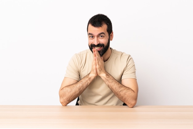 Blanke man met baard in een tafel houdt de palm bij elkaar. Persoon vraagt iets.