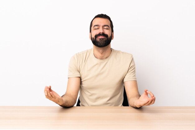 Blanke man met baard in een tafel in zen pose.