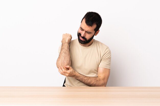 Blanke man met baard in een tafel met pijn in de elleboog