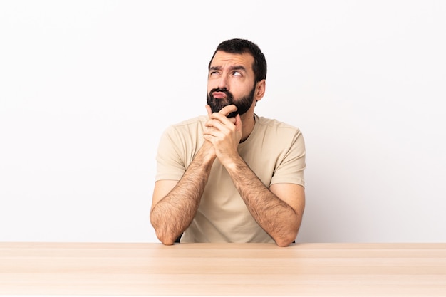 Blanke man met baard in een tafel met twijfels en met verwarde gezichtsuitdrukking.