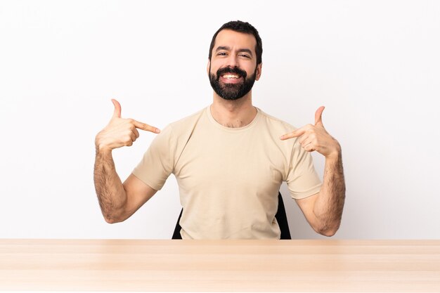 Blanke man met baard in een tafel trots en zelfvoldaan.