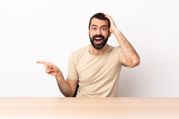 Blanke man met baard in een tafel verrast en wijzende vinger naar de zijkant.