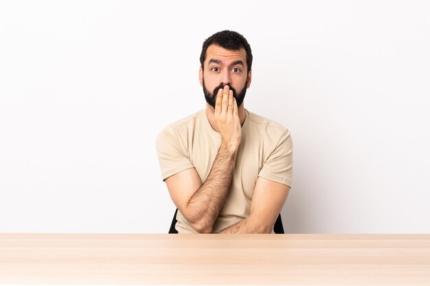 Blanke man met baard in een tafel voor mond met hand.