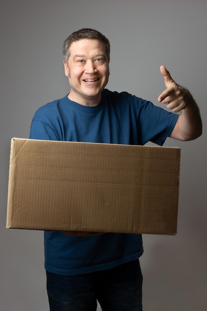 Blanke man met een glimlach wijzend naar de grote bezorgdoos die hij in zijn hand houdt