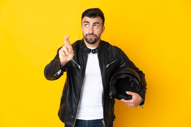 Blanke man met een motorhelm over geïsoleerd geel met vingers die kruisen en het beste wensen