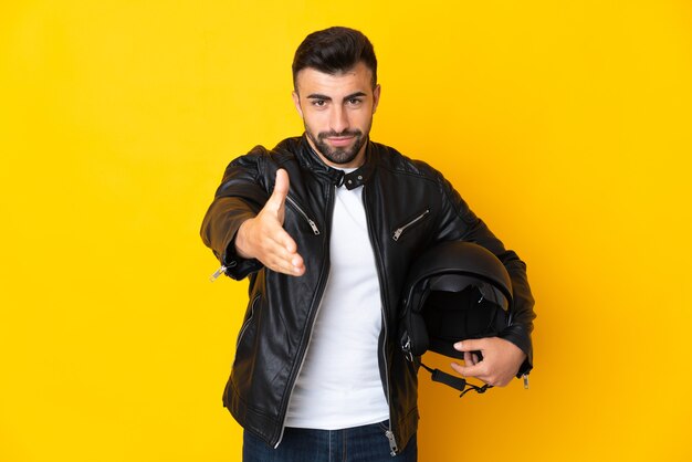 Blanke man met een motorhelm over geïsoleerde gele achtergrond handen schudden voor het sluiten van een goede deal