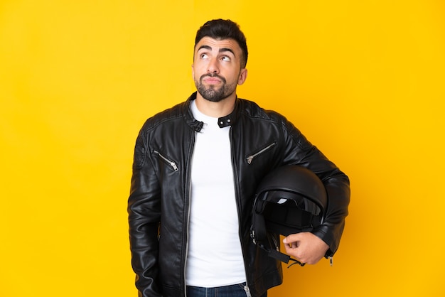 Blanke man met een motorhelm over geïsoleerde gele muur en opzoeken