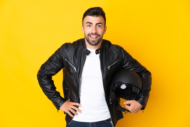 Blanke man met een motorhelm over geïsoleerde gele muur poseren met armen op heup en lachend