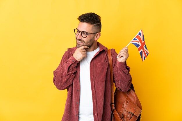 Blanke man met een vlag van het Verenigd Koninkrijk geïsoleerd op geel naar de zijkant kijken en glimlachen