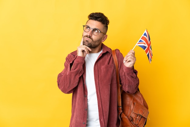 Blanke man met een vlag van het Verenigd Koninkrijk geïsoleerd op gele achtergrond twijfels en denken