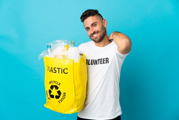 Blanke man met een zak vol plastic flessen om te recyclen geïsoleerd op blauwe achtergrond lachen