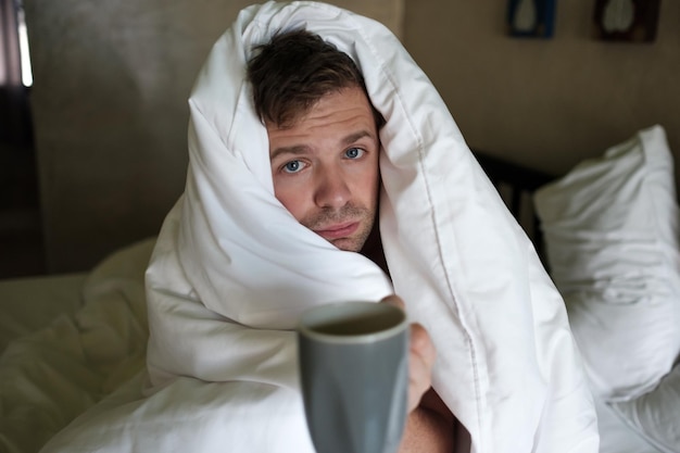 Foto blanke man met slaapgebrek omdat hij griep in bed heeft en om water of medicijnen vraagt