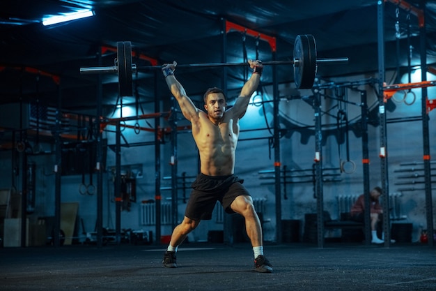 Blanke man oefent in gewichtheffen in de sportschool. Blanke mannelijke sportieve modeltraining met barbell, ziet er zelfverzekerd en sterk uit. Bodybuilding, gezonde levensstijl, beweging, activiteit, actieconcept.