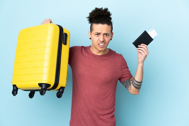 Blanke man over geïsoleerde blauwe muur ongelukkig in vakantie met koffer en paspoort