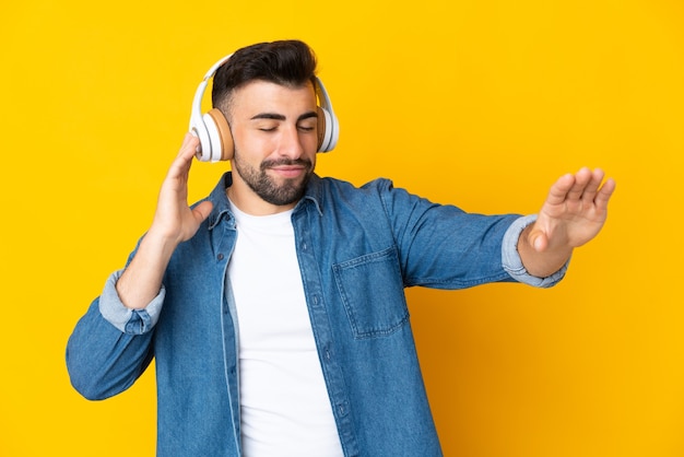 Blanke man over geïsoleerde gele muur muziek luisteren en dansen