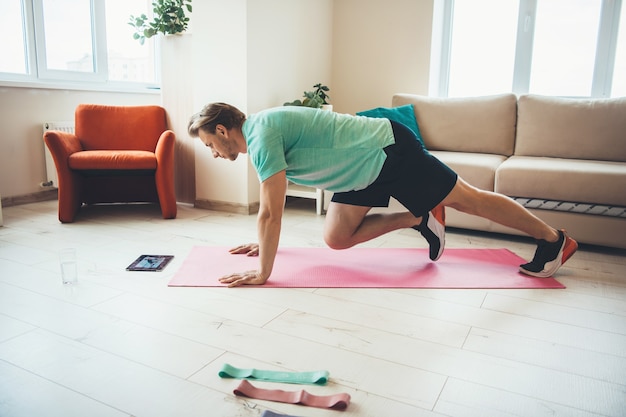 Foto blanke man sport oefeningen thuis terwijl kijken naar de tablet op de vloer