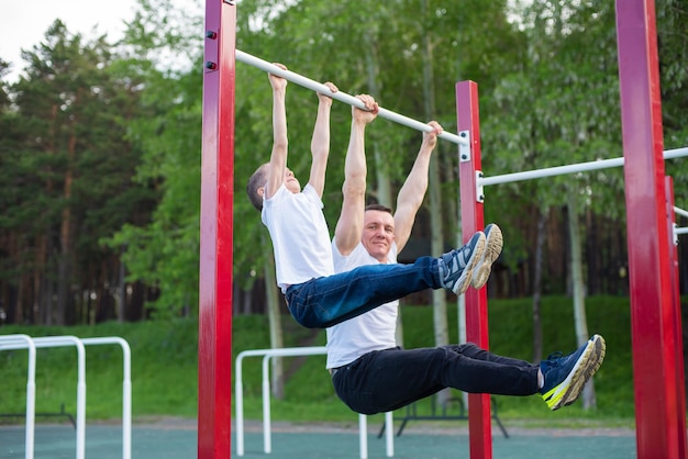 Blanke man traint een jongen op de rekstok op de speelplaats Vader en zoon gaan buitensporten