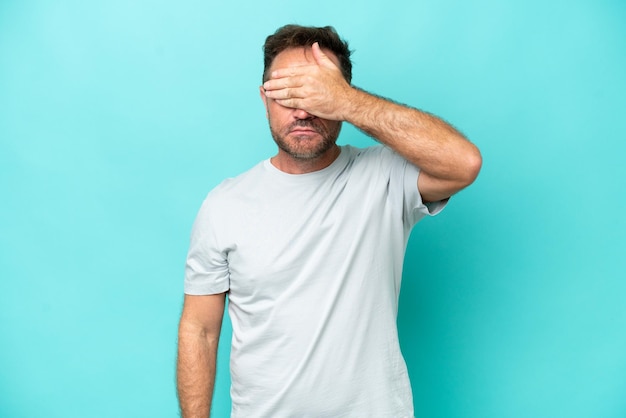 Blanke man van middelbare leeftijd geïsoleerd op blauwe achtergrond die de ogen met de handen bedekt Ik wil niets zien