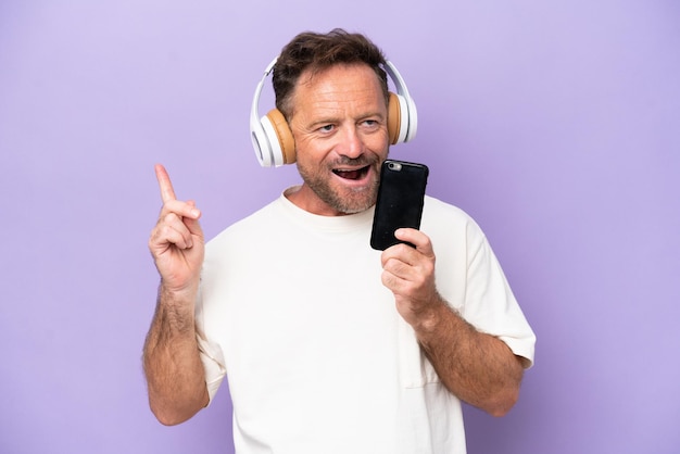 Blanke man van middelbare leeftijd geïsoleerd op paarse achtergrond muziek luisteren met een mobiel en zingen