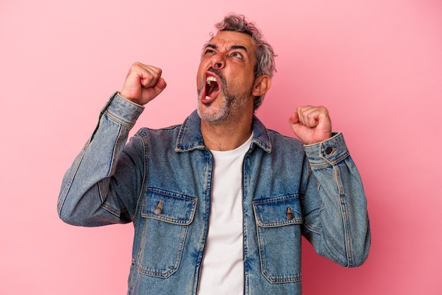 Blanke man van middelbare leeftijd geïsoleerd op roze achtergrond die vuist opheft na een overwinning, winnaar concept.