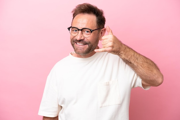 Blanke man van middelbare leeftijd geïsoleerd op roze achtergrond met een bril en telefoongebaar