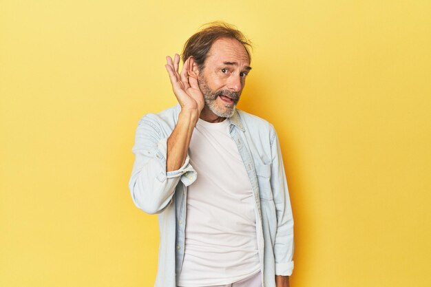 Foto blanke man van middelbare leeftijd in gele studio die probeert te luisteren naar roddels