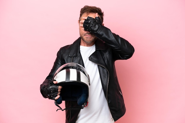 Blanke man van middelbare leeftijd met een motorhelm geïsoleerd op een roze achtergrond die de ogen met de handen bedekt Ik wil niets zien