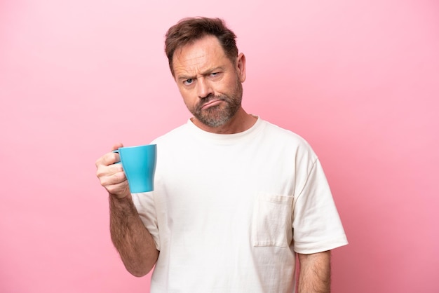 Blanke man van middelbare leeftijd met kopje koffie geïsoleerd op roze achtergrond met droevige uitdrukking