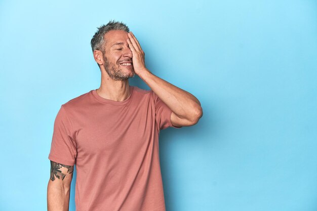 Blanke man van middelbare leeftijd op blauwe achtergrond lachende gelukkige zorgeloze natuurlijke emotie