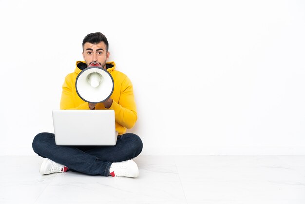 Blanke man zittend op de vloer met zijn laptop schreeuwen door een megafoon