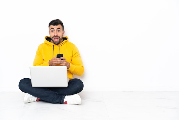 Blanke man zittend op de vloer met zijn laptop verrast en een bericht te sturen