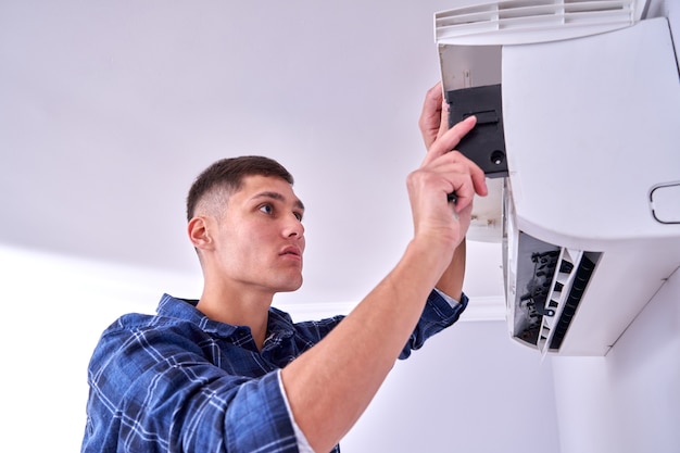 Blanke mannelijke meester in blauw shirt reinigt filters, installeert en repareert airconditioner binnenshuis