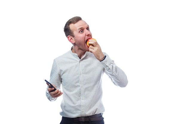 Blanke mannelijke zakenman met een mobiele telefoon in het zwart en een rood-gele appel. Hij draagt een overhemd. Emotioneel portret. Geïsoleerd op witte achtergrond