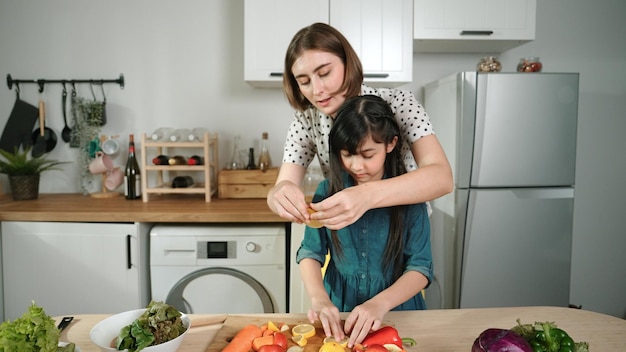 blanke moeder en Aziatisch meisje samen koken en sinaasappel eten Pedagogie