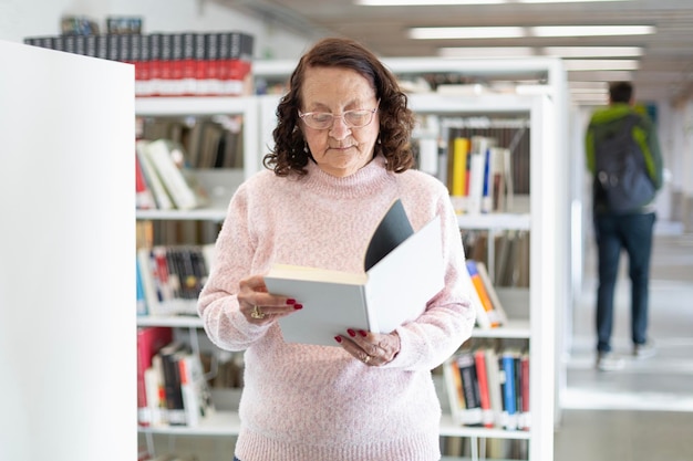 Foto blanke oudere vrouw die een boek leest in een openbare bibliotheek